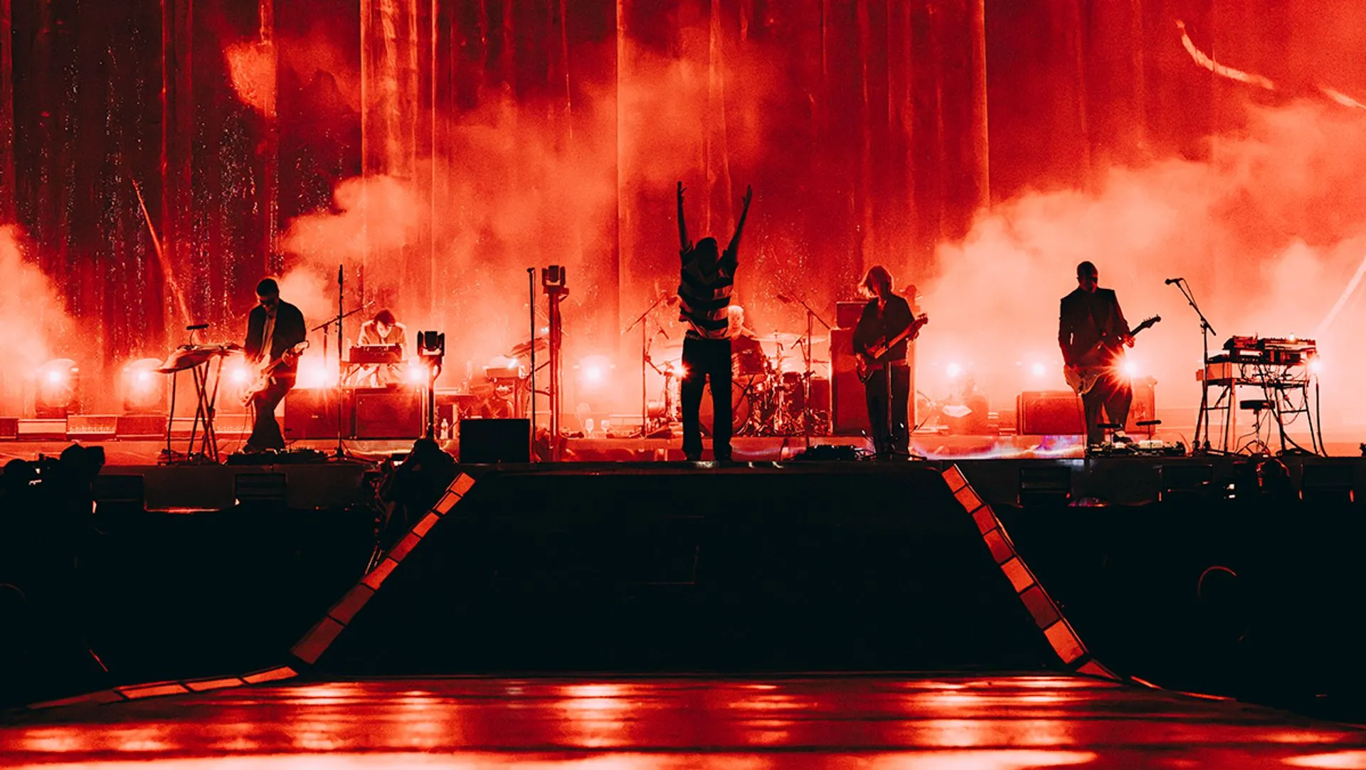 Fontaines D.C. kırmızı ışığa bürünmüş büyük bir festival sahnesinde; solist kollarını havaya kaldırmış